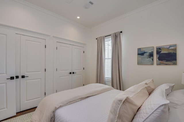 bedroom with hardwood / wood-style floors, two closets, and crown molding