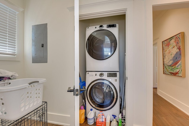 laundry area featuring wood-type flooring, electric panel, and stacked washer and clothes dryer