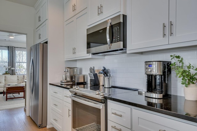 kitchen featuring light hardwood / wood-style flooring, backsplash, dark stone counters, white cabinets, and appliances with stainless steel finishes