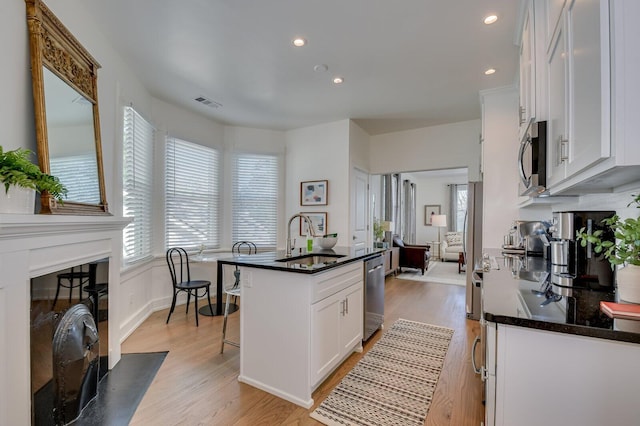 kitchen featuring white cabinets, sink, an island with sink, appliances with stainless steel finishes, and a kitchen bar