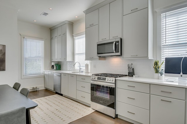 kitchen with decorative backsplash, sink, light wood-type flooring, and stainless steel appliances