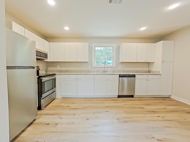 kitchen with white cabinets, sink, stainless steel appliances, and light hardwood / wood-style flooring