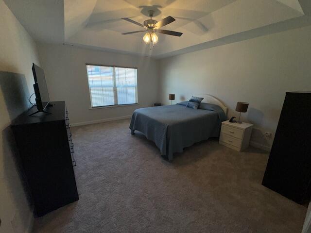 bedroom featuring dark colored carpet, a raised ceiling, and ceiling fan