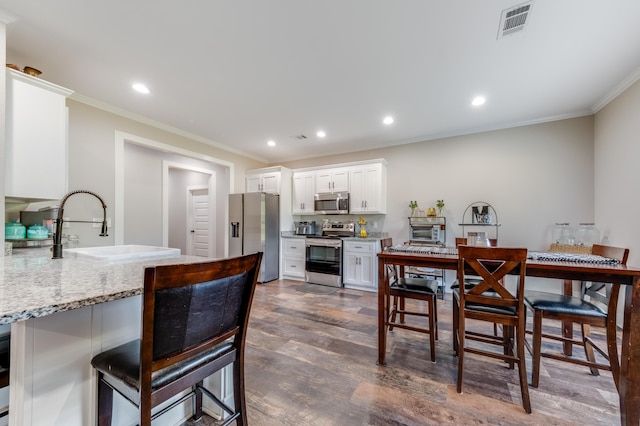 kitchen with dark wood-style flooring, visible vents, a sink, crown molding, and stainless steel appliances