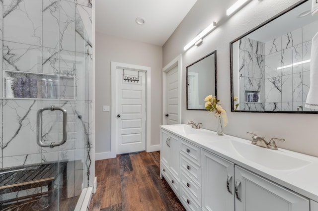 full bathroom with a marble finish shower, double vanity, a sink, and wood finished floors