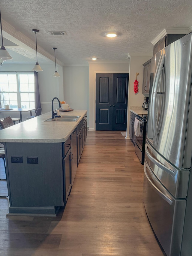 kitchen with dark wood-type flooring, hanging light fixtures, sink, an island with sink, and appliances with stainless steel finishes