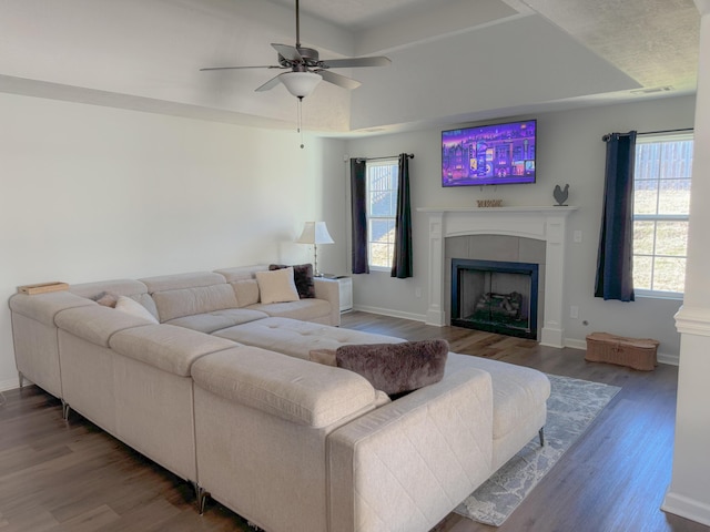 living room featuring a tile fireplace, hardwood / wood-style flooring, a raised ceiling, and ceiling fan