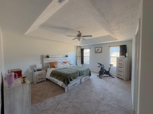 bedroom featuring light carpet, a textured ceiling, a tray ceiling, and ceiling fan