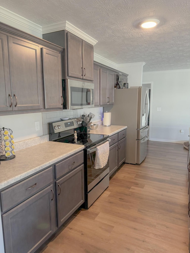 kitchen featuring crown molding, stainless steel appliances, a textured ceiling, and light wood-type flooring