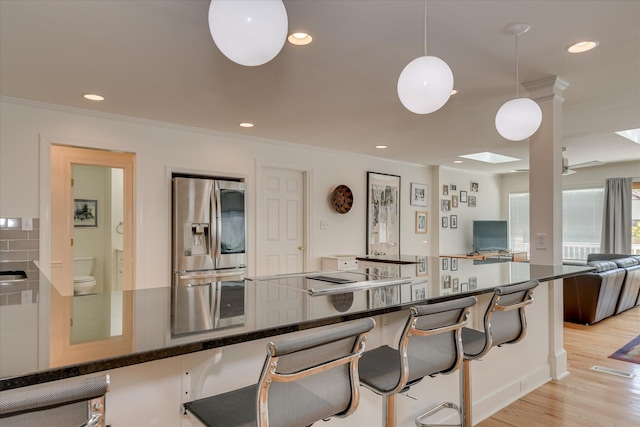 kitchen featuring stainless steel fridge, light wood-style floors, ornamental molding, open floor plan, and a kitchen breakfast bar