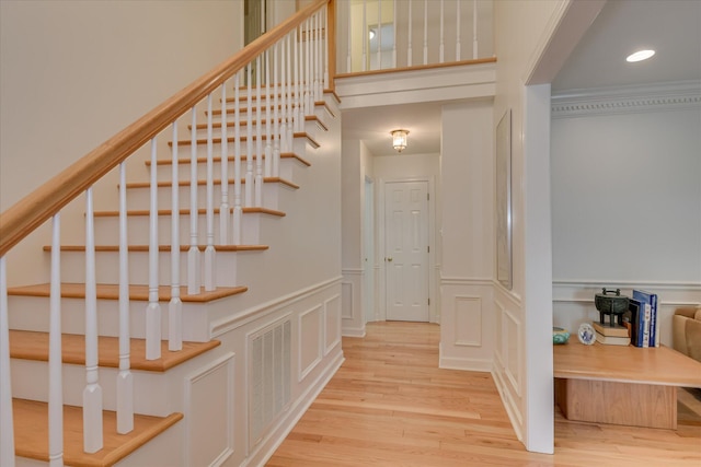 staircase with wood finished floors, a decorative wall, a wainscoted wall, and visible vents