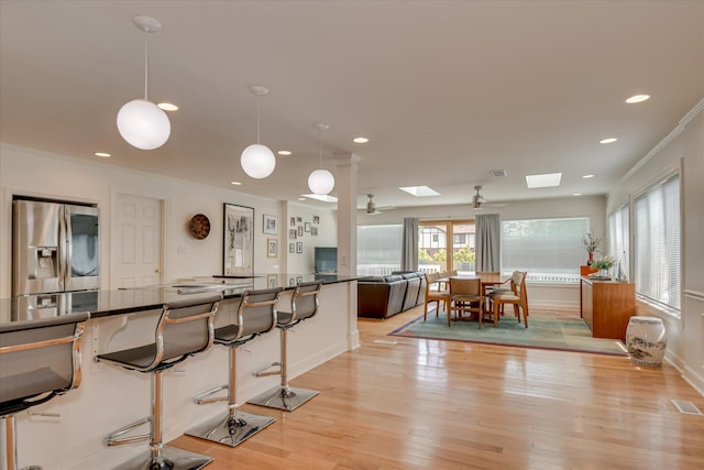 kitchen with recessed lighting, a skylight, stainless steel fridge with ice dispenser, dark countertops, and crown molding