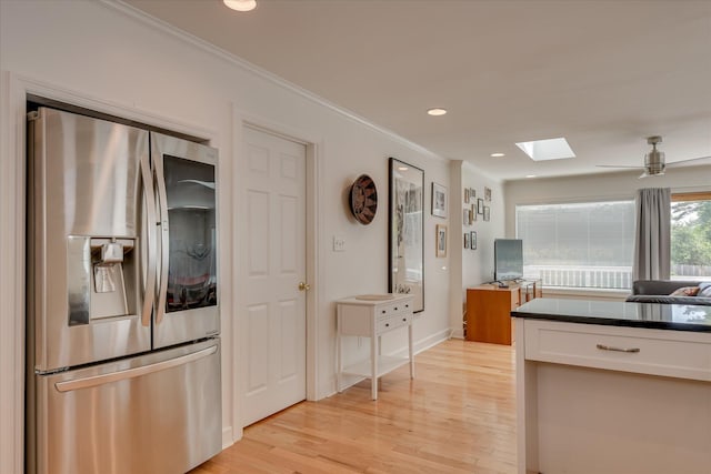 kitchen with a skylight, light wood-style floors, ornamental molding, dark countertops, and stainless steel refrigerator with ice dispenser