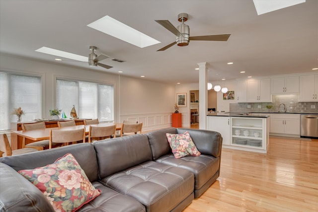 living room with light wood-style floors, ceiling fan, a wainscoted wall, visible vents, and a skylight