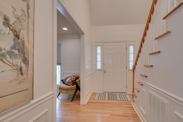 entryway with stairs, light wood-style flooring, a decorative wall, a wainscoted wall, and visible vents