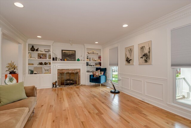 living room with recessed lighting, light wood-style floors, ornamental molding, built in shelves, and a brick fireplace
