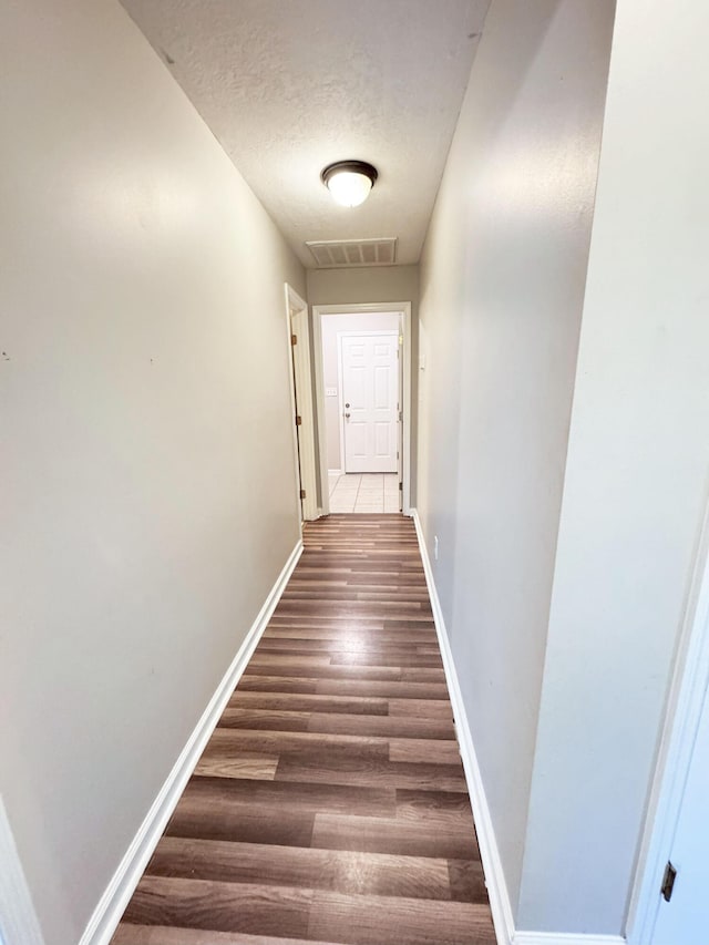 hall with visible vents, baseboards, a textured ceiling, and wood finished floors