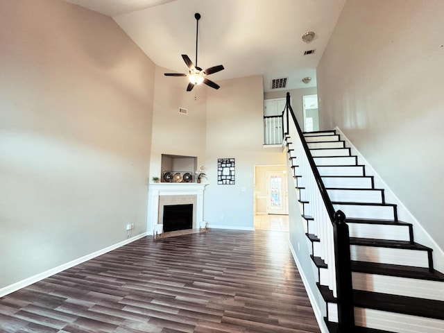 staircase featuring visible vents, a fireplace with flush hearth, wood finished floors, baseboards, and ceiling fan