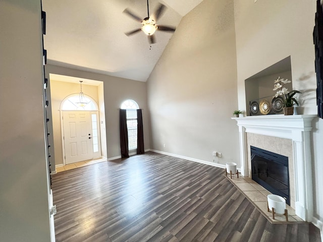 foyer with baseboards, ceiling fan, a fireplace, wood finished floors, and high vaulted ceiling