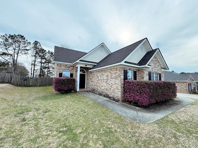 view of side of home featuring a lawn, a shingled roof, brick siding, and fence