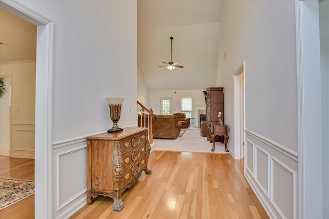 hallway with a towering ceiling, a wainscoted wall, light wood finished floors, and a decorative wall