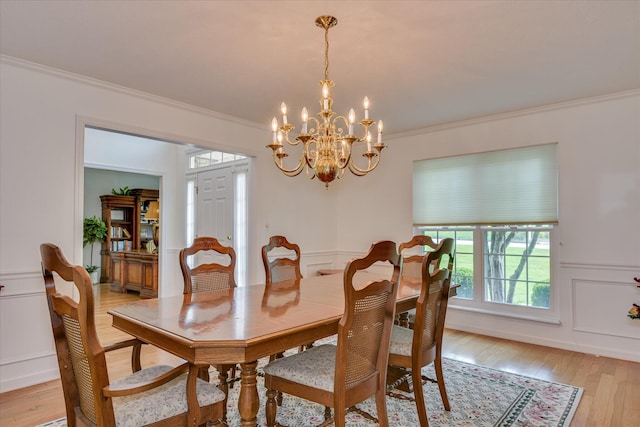 dining area with ornamental molding, wainscoting, light wood finished floors, and a chandelier