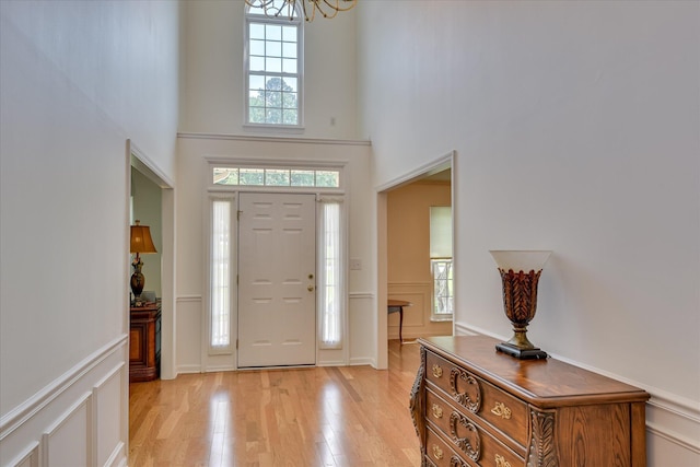 foyer entrance featuring an inviting chandelier, light wood finished floors, a towering ceiling, and a healthy amount of sunlight