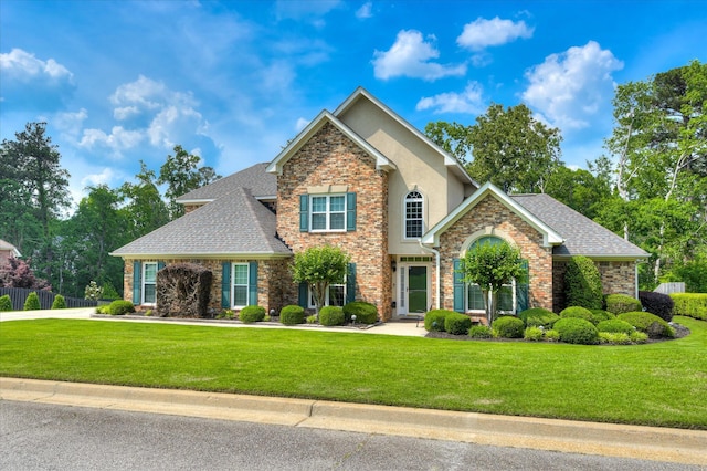 view of front of house featuring roof with shingles, stucco siding, a front yard, and fence