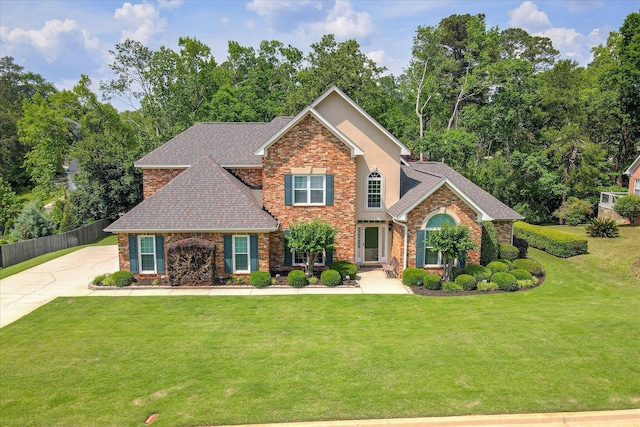 view of front facade featuring brick siding, fence, roof with shingles, and a front lawn