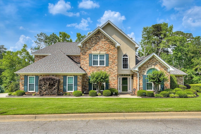 view of front facade featuring stucco siding, a shingled roof, and a front lawn
