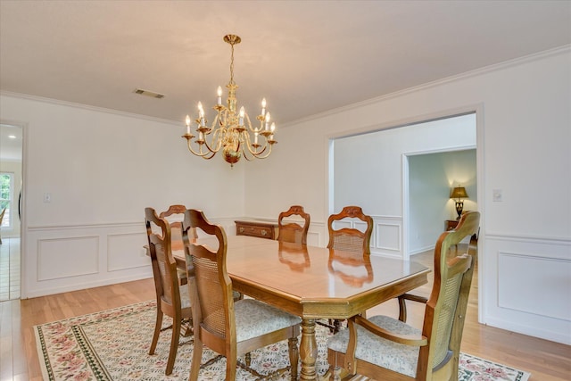 dining area with light wood-type flooring, ornamental molding, a notable chandelier, and visible vents