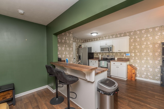kitchen featuring white cabinets, stainless steel appliances, baseboards, dark wood-type flooring, and butcher block counters