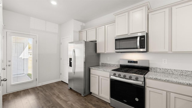 kitchen with white cabinets, appliances with stainless steel finishes, light stone counters, and dark hardwood / wood-style floors