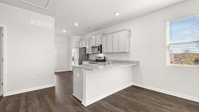 kitchen with sink, light stone counters, stainless steel appliances, dark hardwood / wood-style flooring, and kitchen peninsula