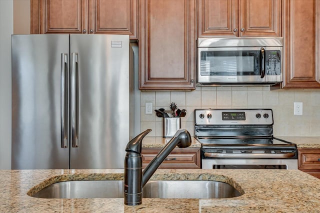 kitchen with a sink, light stone countertops, backsplash, and appliances with stainless steel finishes