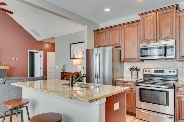 kitchen featuring visible vents, light stone counters, a kitchen breakfast bar, stainless steel appliances, and a sink