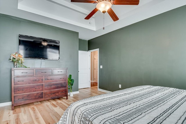 bedroom with a raised ceiling, a ceiling fan, baseboards, and light wood finished floors