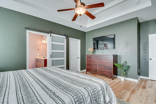 bedroom with light wood-style flooring, a tray ceiling, a barn door, baseboards, and ceiling fan