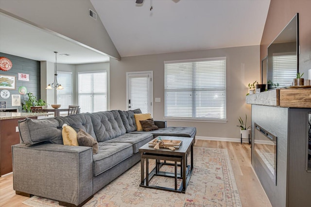 living room featuring visible vents, ceiling fan, lofted ceiling, light wood-style flooring, and a glass covered fireplace