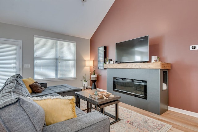 living room with a glass covered fireplace, baseboards, lofted ceiling, and wood finished floors