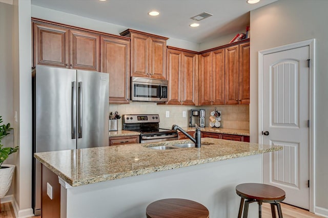 kitchen featuring visible vents, backsplash, light stone countertops, stainless steel appliances, and a sink