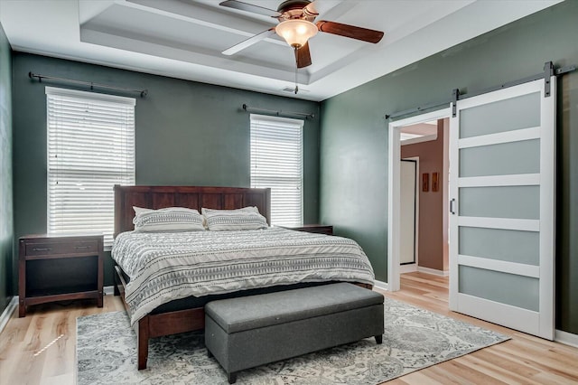 bedroom featuring a ceiling fan, baseboards, a tray ceiling, light wood-style floors, and a barn door