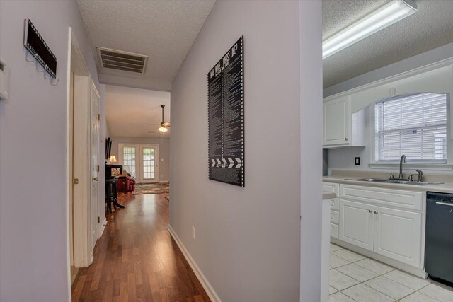 hallway featuring a sink, visible vents, light wood-type flooring, and a textured ceiling