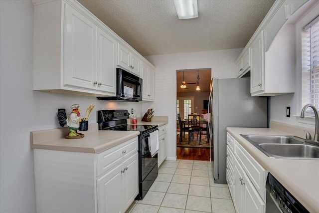 kitchen with light tile patterned floors, light countertops, white cabinets, black appliances, and a sink