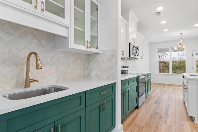 kitchen featuring white cabinets, a sink, stainless steel appliances, light countertops, and green cabinetry