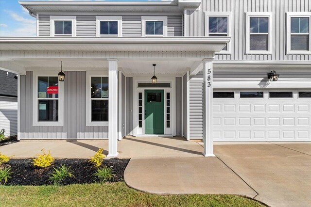 doorway to property featuring an attached garage, driveway, a porch, and board and batten siding