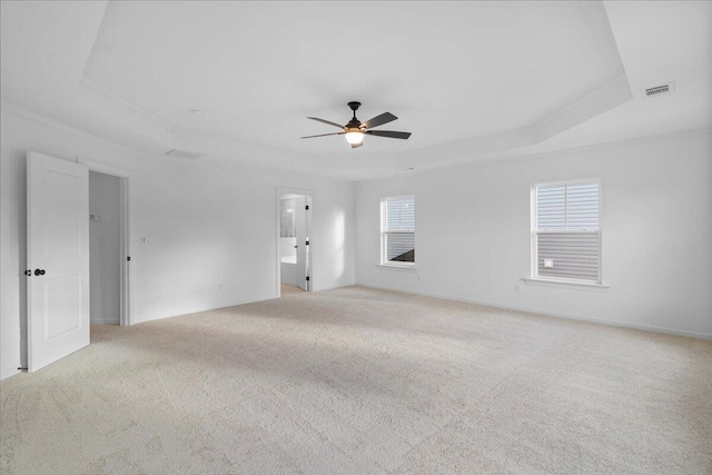 empty room with visible vents, a raised ceiling, baseboards, light colored carpet, and ceiling fan