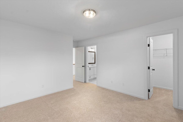 unfurnished bedroom featuring connected bathroom, light colored carpet, baseboards, a spacious closet, and a closet