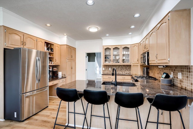 kitchen with glass insert cabinets, dark stone countertops, appliances with stainless steel finishes, a peninsula, and a sink