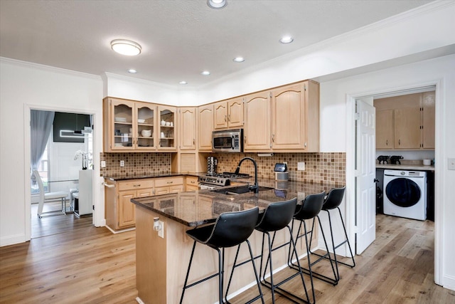 kitchen featuring a kitchen breakfast bar, washer / clothes dryer, light brown cabinets, and appliances with stainless steel finishes